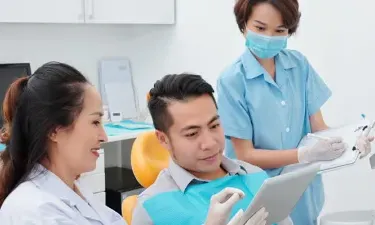 Dental assistant with diploma helping dentist consult with patient